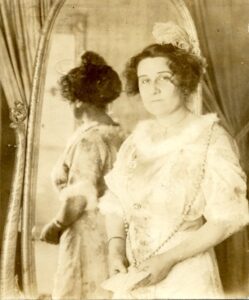 historical photo of a woman standing in front of a mirror looking toward the camera